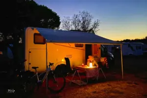 Frau sitzt vor dem Wohnmobil bei Abendstimmung mit stimmungsvoller Beleuchtung.