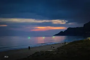 Fischer mit beleuchteter Rutenspitze stehen am Strand in der Abenddämmerung in Erwartung eines tollen Fangs.