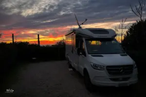 Wohnmobil steht vor dem Strand mit wunderschönem Sonnenutergang im Hintergrund.