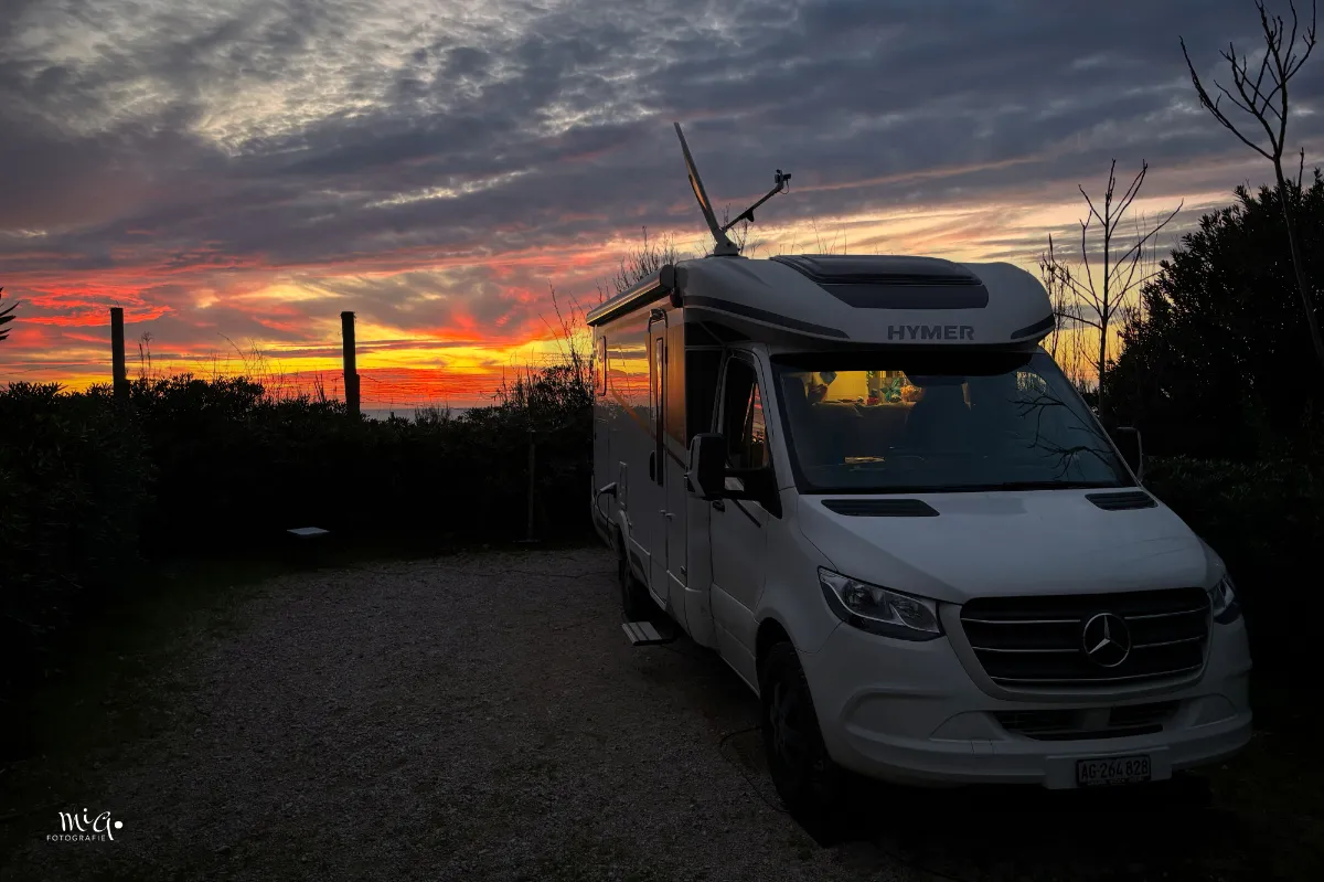 Wohnmobil steht vor dem Strand mit wunderschönem Sonnenutergang im Hintergrund.