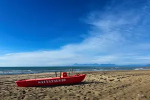 Ein rotes Rettungsboot liegt im Sand am Strand und wartet auf seinen Einsatz.