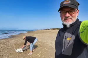 Zwei Menschen mit einem Hund spazieren am Strand und spielen mit dem Hund.