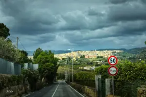 Dunkle, schwere Wolken hängen über der Strasse, nur das voraus liegende Städtchen wird von der Sonne beschienen und leuchtet in der Landschaft