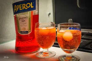 Zwei Gläser gefüllt mit Aperol-Spritz und Eiswürfeln stehen neben der Aperol Flasche
