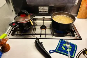 Zwei Pfannen auf dem Kochherd, eine mit Tomatensauce die andere mit Spaghetti