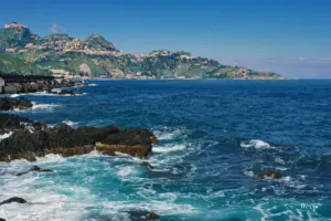 Blick über das tiefblaue Meer von Giardini Naxos nach Taormina das majestätisch auf den Hügeln über dem Meer thront.