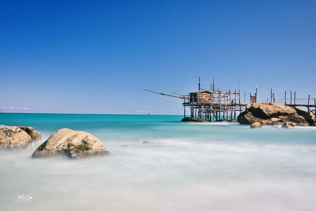 strand-meer-wasser-fischerhaus Ein Blick über die im Wasser liegenden Felsen führt zum Trabocco, dem Fischerhaus das auf Holzpfählen im Wasser steht.