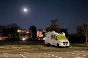 Wohmbil steht parkiert auf einem Parkplatz in der Nacht und der Mond leuchtet am Himmel.