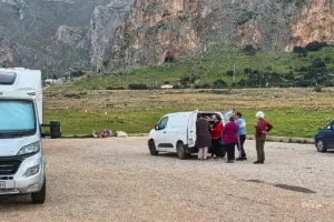 Mehrere Personen stehen hinter einem Auto am warten im Hintergrund die mächtigen Berge