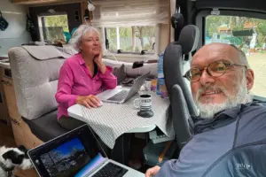 Eine Frau und ein Mann sitzen im Wohnmobil am Tisch und arbeiten an ihren Laptops.