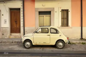 Ein uralter, reichlich rostiger Fiat 500 steht vor dem Haus parkiert und wartet auf die nächste Fahrt