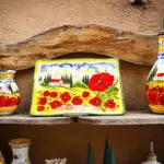 An der Aussenwand eines Handwerkskunst Ladens ist schönes, handgemaltes Tongeschirr ausgestellt. Bemalt mit Mohn und den typischen toskanischen Zypressen.