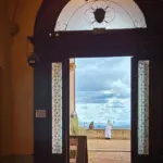 Ein Blick durch eine grosse Türe auf einen Aussichtsbalkon zeigt eine Nonne in ihrer Tracht die mit dem Handy am fotografieren ist.