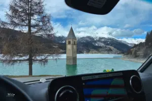 Blick aus dem Wohnmobil Cockpit auf den teilweise noch gefrorenen Reschensee mit dem aus dem See harausragenden Kirchturm.