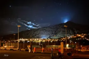 Scuol bei Nacht, auf den Bergen sieht man das Licht der Berghütte und über dem Bergrücken steht die Mondsichel zur Dekoration des Sternenhimmels.