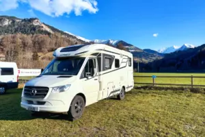 Ein Wohnmobil steht auf der Wiese parkiert inmitten der umliegenden hohen Berge.