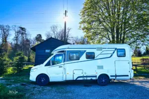 Wohnmobil steht parkiert vor einem Vereinshaus am Waldrand.